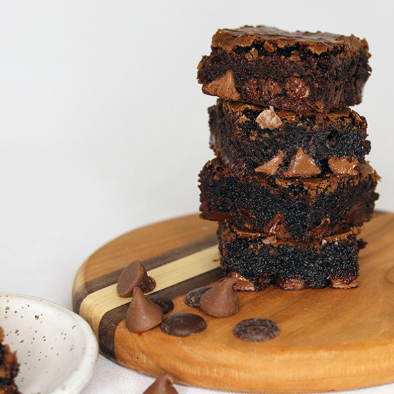 A stack of fudgy cocoa brownies on a round wooden board against a white background