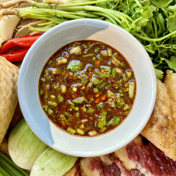 Jeow bee, a sour Lao dipping sauce, surrounded by grilled beef, fresh vegetables, and chilies.
