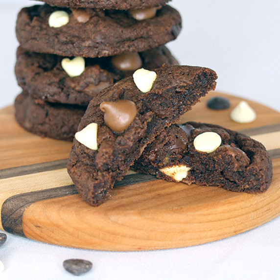 Stack of triple chocolate cookies on a round wooden board, front cookie broken open.