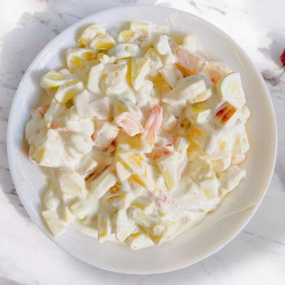 Fruit cocktail salad arranged in white bowl on white marble countertop.