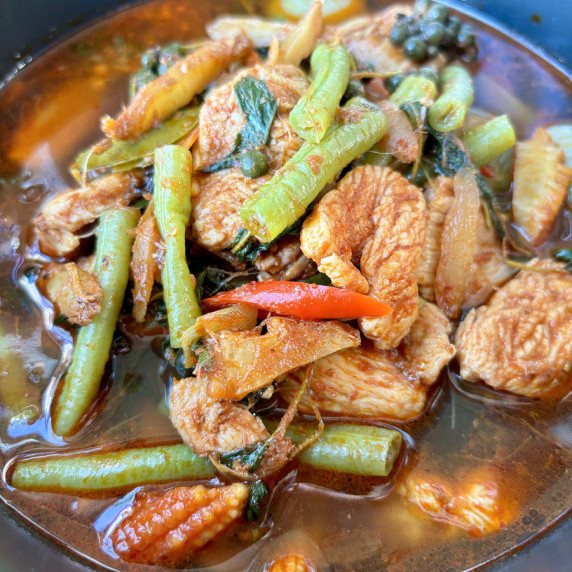 Thai jungle curry, kaeng pa, with vegetables and protein in a black bowl.