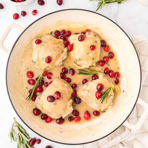 creamy cranberry chicken in a white skillet with rosemary garnish