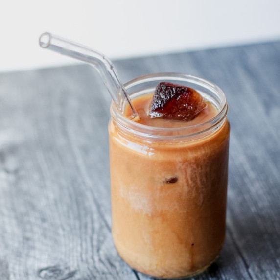 Iced coffee in a glass with glass straw on top of a color gray wood-like countertop