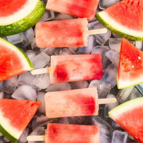 A close up view of watermelon popsicles and slices of watermelon on a tray full of ice.