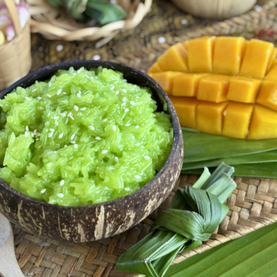 Mango sticky rice served in a coconut shell, with a ripe mango next to it.