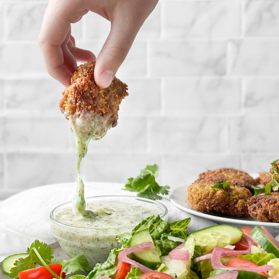 A hand dipping a falafel in the dairy free tzatziki dip.
