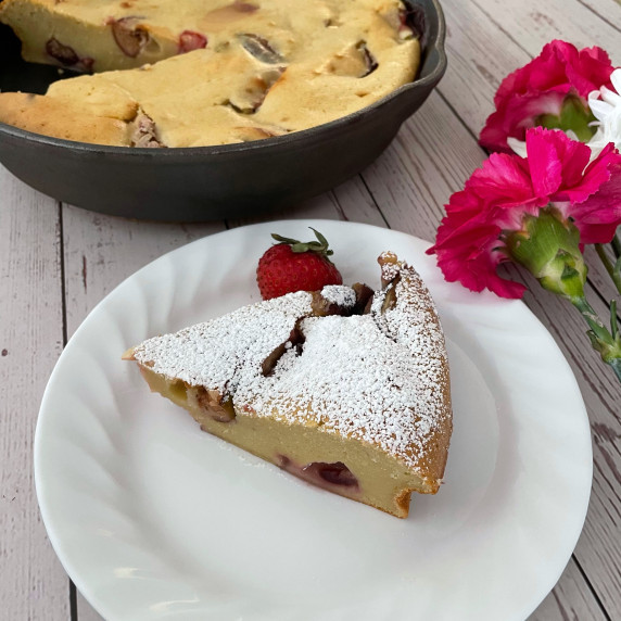 Clafoutis in a cast iron skillet with a slice cut out and on a white plate to the size.