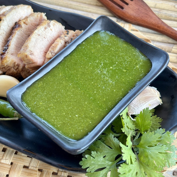 Green cilantro sauce served sauce in a saucecup with a side of sliced meat.