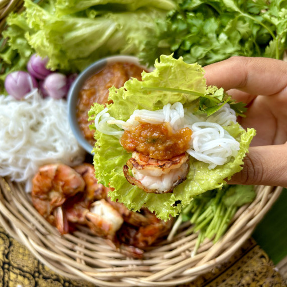 Hand holding a Thai shrimp lettuce wrap with rice vermicelli, peanut sauce, and shrimp.