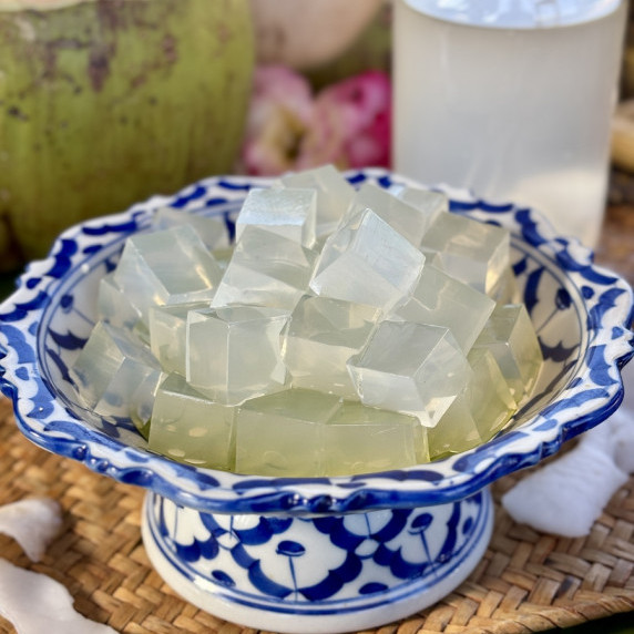 Thai coconut jelly cubes in a traditional with bowl fresh coconut water in the distance.