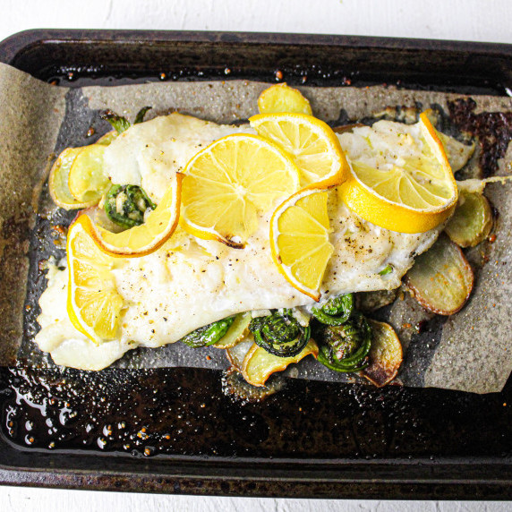 bright yellow lemons are layered over a fish fillet with green fiddlehead ferns peaking out.