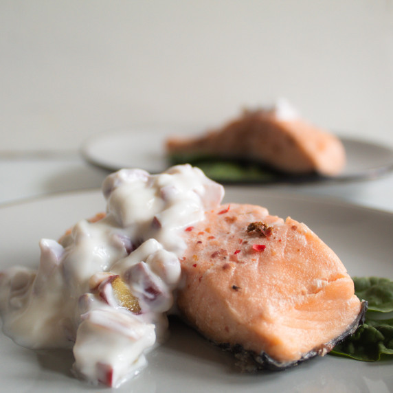 pink salmon fillet sits on green lettuce leaves, with white rhubarb yogurt sauce drizzled over