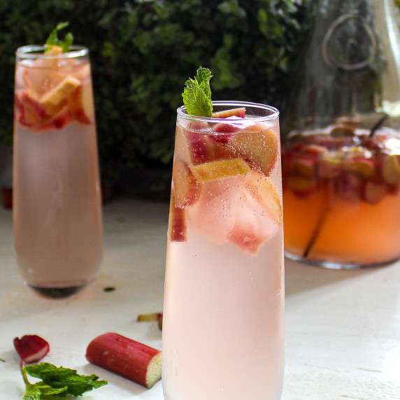 tall glasses filled with light pink rhubarb cocktail, topped with green mint leaves. 
