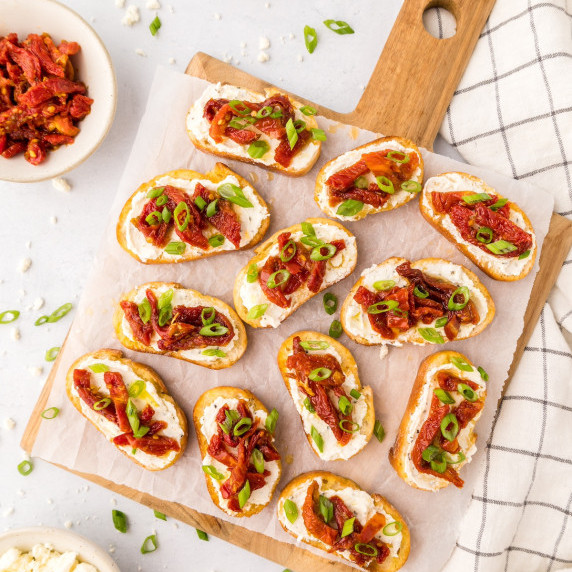 sun-dried tomato crostini on a cutting board with feta cheese and green onions