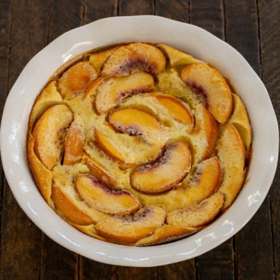 Overhead view of peach clafoutis in a white ceramic dish.