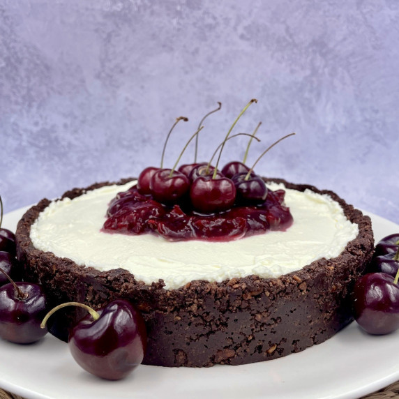 A cherry cheesecake with cherry sauce and fresh cherries on a serving plate