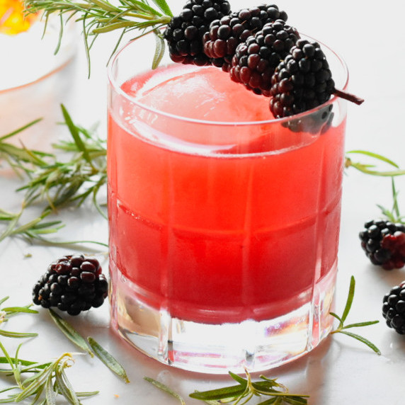 Waterford crystal with round ice cube, bright cocktail, 4 blackberries on rosemary branch