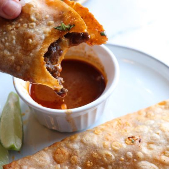 Cheesy brisket taco dipped into enchilada sauce with lime