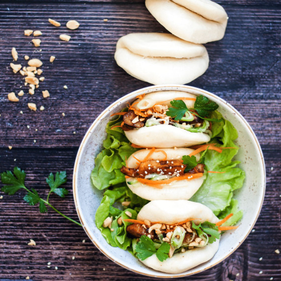 Steamed bao buns with chicken teriyaki filling in a white bowl and a wood countertop