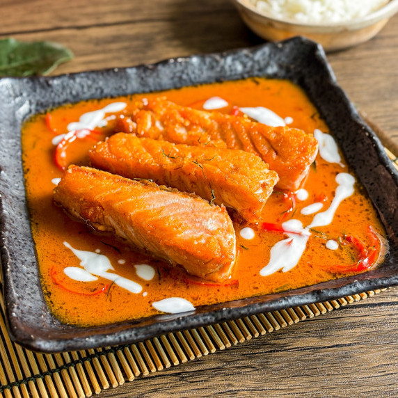 Close-up of choo chee salmon with coconut milk, red chilies, and strips of kaffir lime leaves.