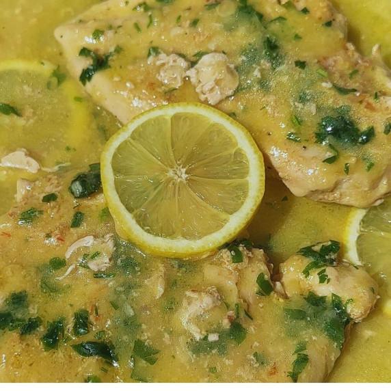 Two pieces of chicken breast with lemon sauce and garnished with parsley