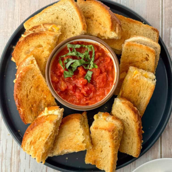 Plate with small appetizer sized grilled cheese sandwiches with tomato dipping sauce