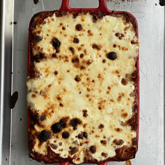 Bubbly cheese lasagna in a red pan on a cookie sheet