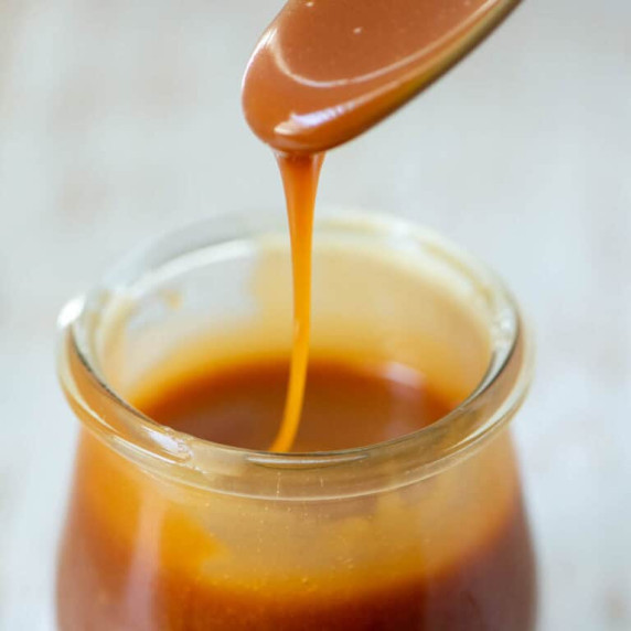 Photo of homemade salted caramel sauce dripping off a spoon into a jar 