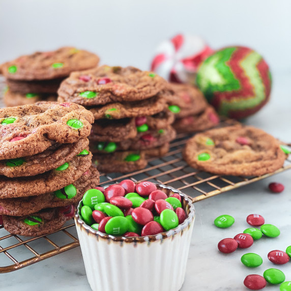 Stacks of M&M chocolate chip cookies on a cooling rack, and a bowl of red and green m&ms