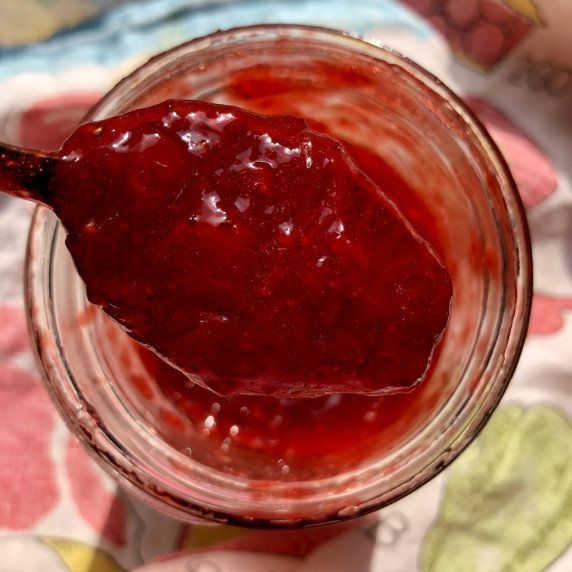 A large spoon filled with bright red strawberry jam.