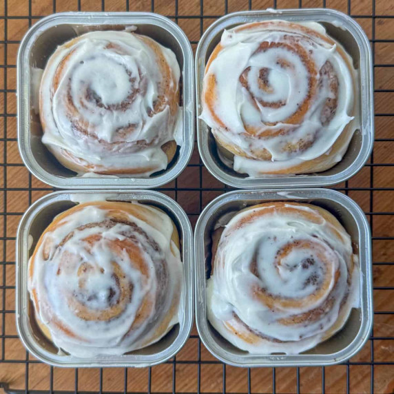 Four individual cinnamon rolls in square aluminum baking cups on a cooling rack 