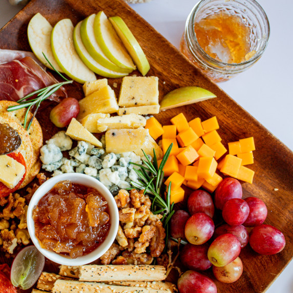 cheese board with apple cider jam in center.