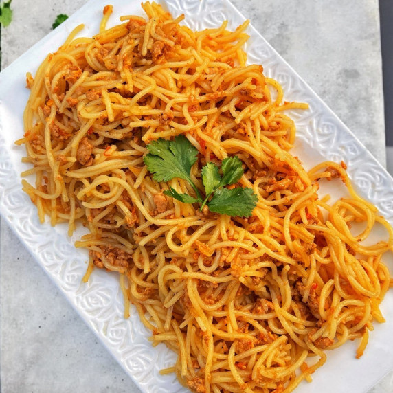 Minced chicken spaghetti arranged in a white tray placed on concrete countertop 