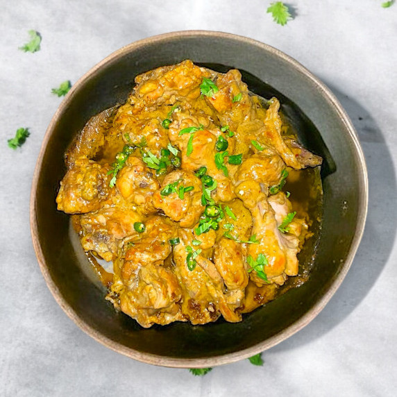 Dahi chicken karahi arranged in black bowl placed on concrete countertop 