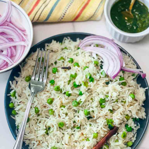 Green peas and white rice served with green chutney and sliced onion on side in a blue plate 