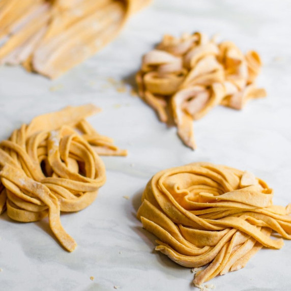 Fresh pumpkin pasta made from two ingredients is laid in small bundles on a marble countertop.