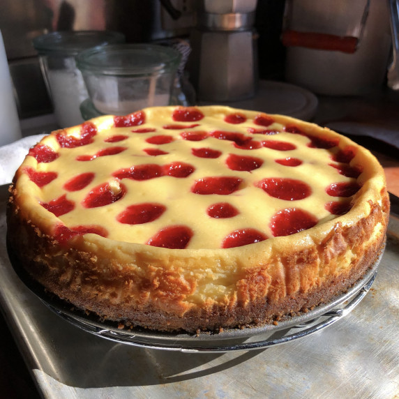 Strawberry cheesecake with thick Biscoff cookie crust w/a bite on a fork and slice on the plate.