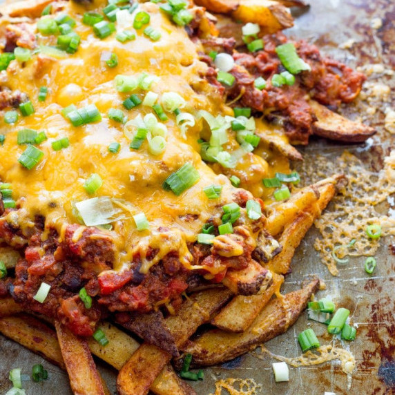 Homemade chili cheese fries piled high on a baking sheet and garnished with sliced scallions.