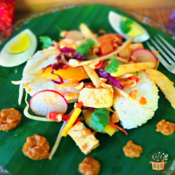 Indonesian gado gado salad with spicy peanut sauce, rice cakes, eggs and vegetables on a banana leaf