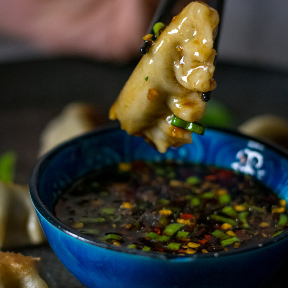 Vegan gyozas filled with mushroom and kale are being dipped in a sesame dip. 