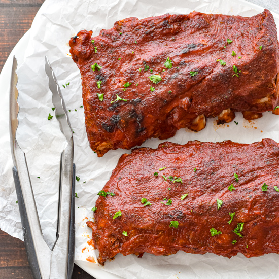 two racks of bbq pork ribs on white parchment paper with tongs