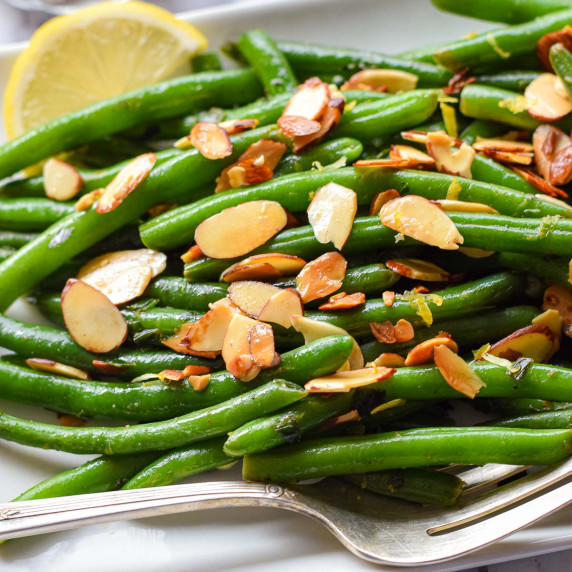 grean beans covered in toasted almonds on a white plate.