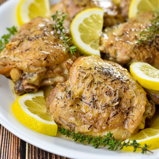 instant pot lemon chicken thighs on a white platter garnished with lemon slices and thyme sprigs