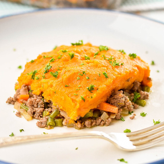 a square piece of sweet potato shepherd's pie on a white plate with a fork