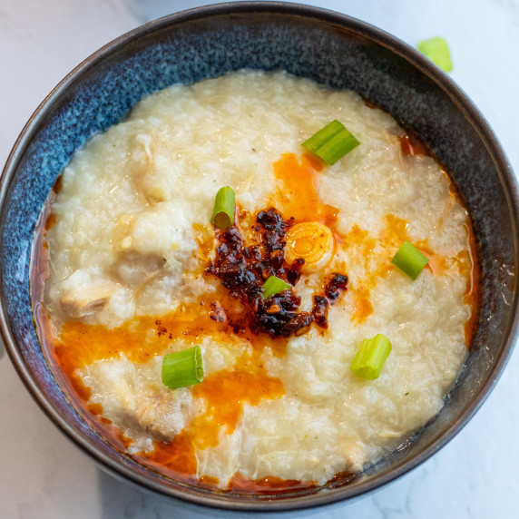 Chicken congee in a brown color bowl with chilli oil and green onions on top