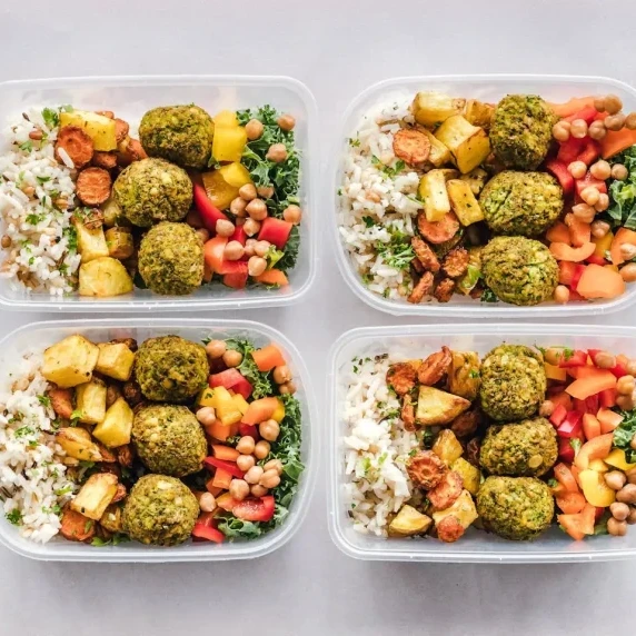 A healthy meal prep featuring containers with falafel, roasted vegetables, rice, and fresh chickpea 