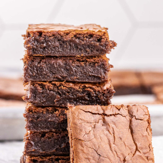Six Irresistible Chewy Gooey Brownies squares on top of each other over parchment paper.