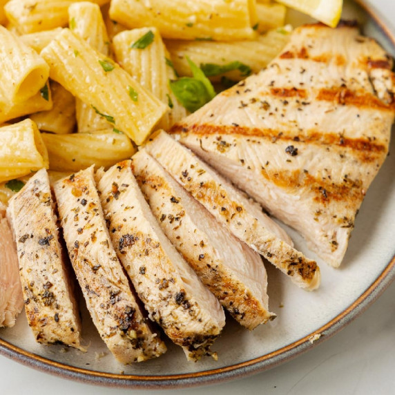 Grilled chicken slices on a plate with rigatoni pasta on a plate.