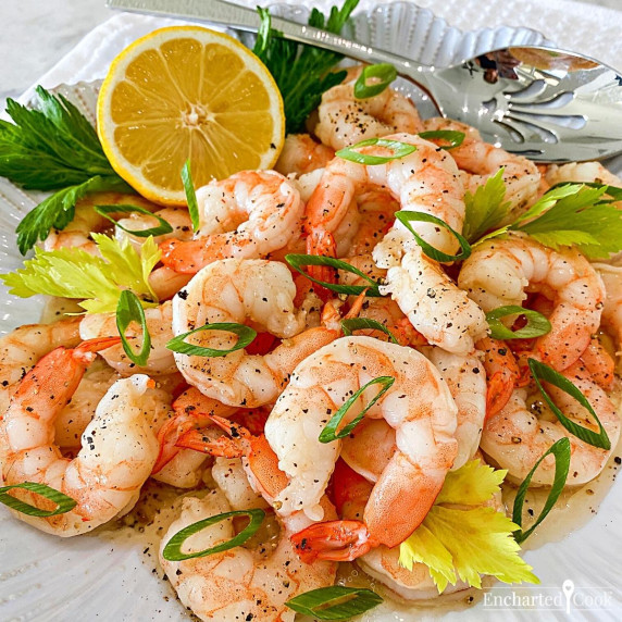 Cooked shrimp in a marinade with sliced green onions on a white plate.
