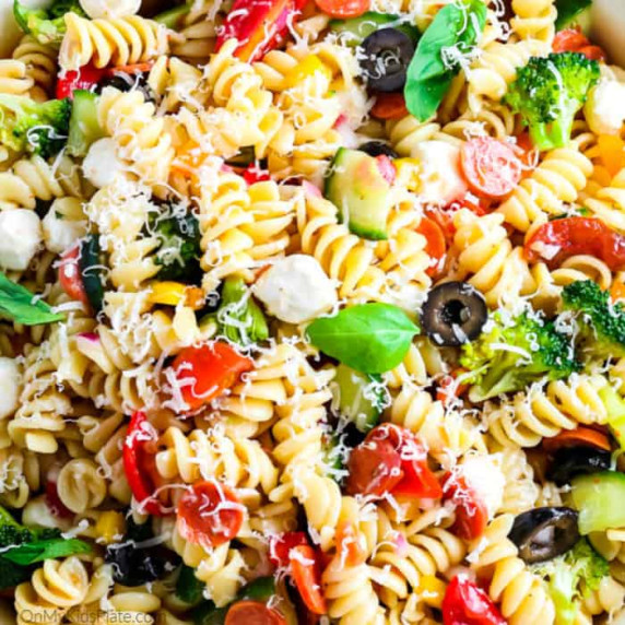 Close up view of pasta full of cheese, basil, pepperoni and olives for an Italian pasta salad. 